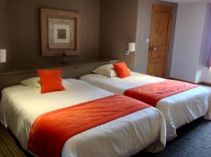 two beds in a hotel room with orange pillows at Hôtel La Gibecière in Lohéac