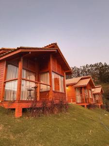 a log cabin on a grassy hill with two houses at Domus Fiorese Chalés in Venda Nova do Imigrante