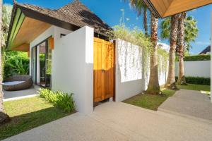 une maison avec une porte en bois et des palmiers dans l'établissement Anchan Villas Phuket - Private 2 Bedroom Pool Villas by Escape Villas, à Ban Phru Champa