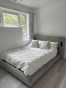 a bed in a white bedroom with two windows at Newly Refurbished - Stylish - Modern - And Cosy Flat - King Size Bed with Built In Speakers - Bedside Lamp - And USB Ports - Sofa Bed - In Islington North London in London