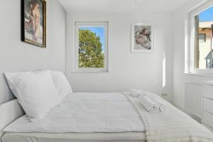 a white bedroom with a bed and two windows at Pełczyńskiego Comfort Stay by Solarento in Warsaw