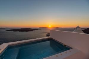a swimming pool with the sunset in the background at Aesthesis Boutique Villas Fira in Fira