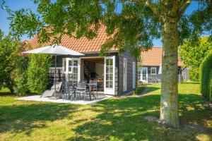 a house with a patio with an umbrella and chairs at Gezellige Zeeuwse Cottage voor 4 personen in Wemeldinge