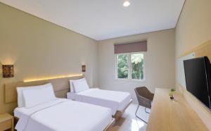 a hotel room with two beds and a flat screen tv at Pelangi Hotel at Artotel Pelangi Park in Pasirkuda
