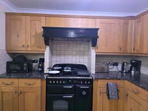 a kitchen with a black stove and wooden cabinets at North London Holiday home, Driveway Parking, BBQ and Indoor Jacuzzi hot tub in Brimsdown Station +11 photos