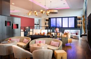 a lobby with couches and tables and a tv at Leonardo Royal Hotel Munich in Munich