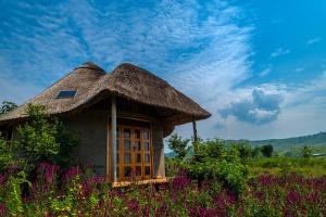 una choza con techo de paja en un campo de flores en Nzoghu Heritage Safari Camp, en Kasese