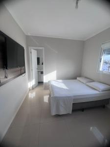 a white bedroom with a bed and a flat screen tv at IJUÍ APART HOTEl in Ijuí