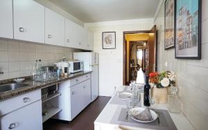 Una cocina con gabinetes blancos, un fregadero y un microondas. en Apartamento T3 perto do Centro do Porto, Check-in 24 horas,Cozinha totalmente equipada, Wi-Fi 44Mbps, Propriedade Confortável e Espaçosa, Com Vaga de Carro Pública, Adequada para famílias, hóspedes em negócios e grupos de amigos e nomades digitais, en Oporto