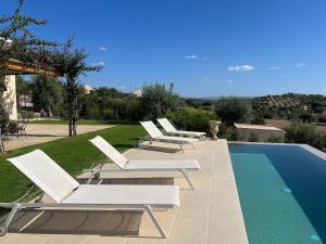 a row of white lounge chairs next to a swimming pool at Villa Heron Sicily in Noto