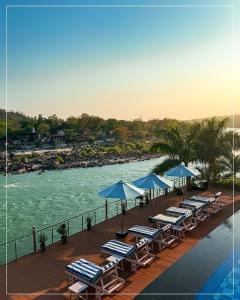 a deck with lounge chairs and umbrellas next to a body of water at Divine Resort & Spa in Rishīkesh