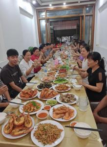 un grupo de personas sentadas en una mesa larga con platos de comida en Nhà nghỉ Bình Liên, en Sầm Sơn