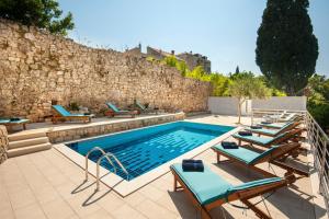 a pool with chaise lounge chairs next to a stone wall at California Apartments in Dubrovnik