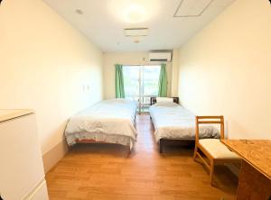 ein Zimmer mit zwei Betten und einem Tisch darin in der Unterkunft ハイ沖縄金武店トイレお風呂共用 プレオープン中駐車場有 ペット同伴可能長期滞在可能2025年10月より車貸し出しサービス有希望であればお申し付けください in Kin