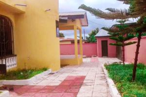 a yellow and pink house with a palm tree and a sidewalk at Oheneba Guest House in Dormaa Ahenkro
