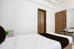 a bedroom with a white bed and a wooden door at Hotel O Metro in Rajkot