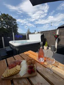 a picnic table with cheese and wine glasses and a hot tub at Pauls Place - Festive Cottage with Hot Tub in Brynsiencyn