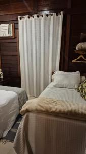 a bedroom with two beds and a white curtain at Chalé Oxossi in Maricá