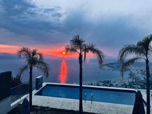 a swimming pool with palm trees and a sunset at Villa e Diellit in Kaninë