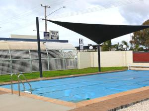 a large swimming pool with a large umbrella over it at Charles Sturt Motor Inn in West Wyalong