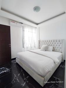 a large white bed in a white room with a window at Leboss Meublé in Yaoundé