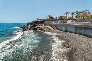 a beach with the ocean and buildings and palm trees at Apartamento Refugio del Mar in Candelaria