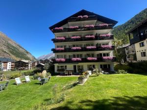 a large building with chairs and flowers in a yard at Hotel Adonis in Zermatt