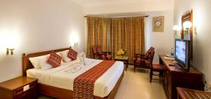 a hotel room with a bed and a desk and a television at KrishnaInn in Guruvāyūr
