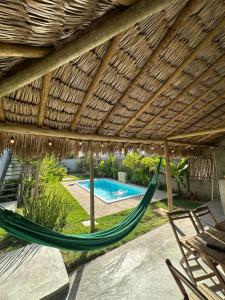 a hammock under a thatched roof with a swimming pool at Morada do Vento in Guriú
