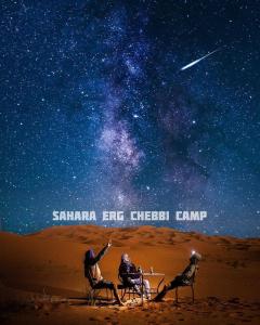 Tres personas sentadas en el desierto mirando las estrellas en Sahara Erg Chebbi Camp, en Merzouga