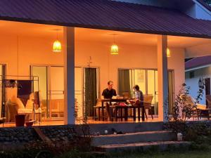 two people sitting at a table on the porch of a house at Creek Cottage Chaeson in Ban Mun Thung