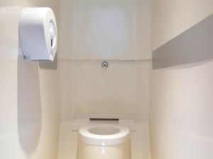 ein weißes Bad mit einem WC und einem Papierspender in der Unterkunft hotelF1 Valenciennes Douchy les Mines in Haulchin