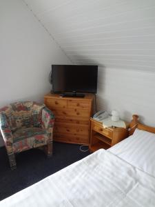 a bedroom with a bed and a tv and a chair at Hotel-Pension Stöber in Jever