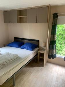 a bedroom with a bed with blue pillows and a window at Chalets van Minicamping De Braamhof in Koudekerke