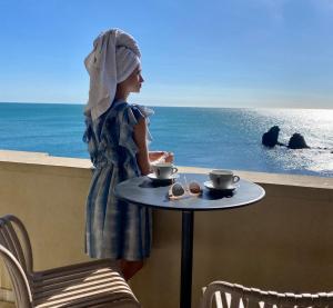 阿格德角Hôtel La Grande Conque的一位女士站在阳台上，桌子上放着杯子