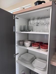a cupboard with plates and bowls and wine glasses at La Petite Hortense in Conteville