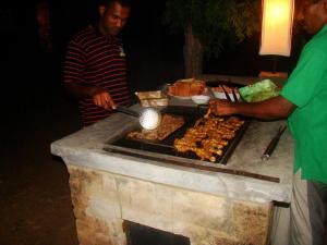 two men are cooking food on a grill at Panthera Lodge Yala in Kirinda