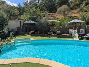 a swimming pool in a yard with chairs and umbrellas at La cabane des Pachous in Tourves