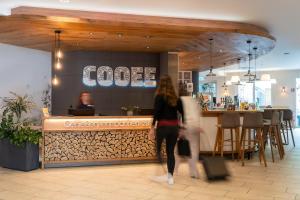 a woman walking past a bar in a restaurant at COOEE alpin Hotel Bad Kleinkirchheim in Bad Kleinkirchheim