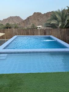 a large blue swimming pool next to a wooden fence at Alhara Lodge استراحة الحارة in Hatta