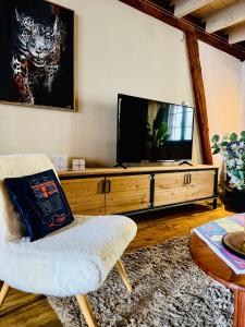 a living room with a tv and a white chair at La Maison Rouge Au coeur de la ville. in Riquewihr