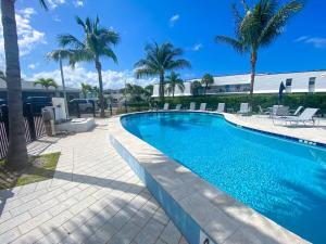 a swimming pool with palm trees and a building at Stylish Coastal Studio Walk to Beach, Pool & Eats in Riviera Beach