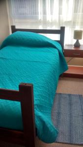 a bed with a green comforter and a window at Departamentos Rohe in Puerto Montt