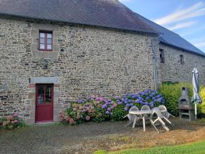 a stone building with two chairs and a table and flowers at La Maison Bienvenüe - Baie du Mont Saint Michel in Baguer-Pican
