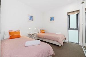 a bedroom with two beds with orange pillows and a window at Cotton Beach 97 Luxurious Mid Floor Apartment in Casuarina +19 photos