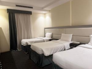 Una habitación de hotel con tres camas con sábanas blancas. en Shouel Inn Furnished Apartments, en La Meca