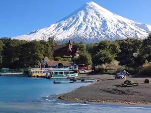 a snow covered mountain in the distance with a house and a river at Hostal Brisas del Sur in Puerto Varas