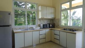 a kitchen with white cabinets and a microwave and two windows at Diyar Villas Puncak NB3/3 in Puncak