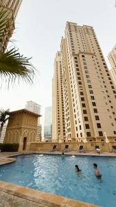 Dos personas nadando en una piscina con edificios altos en Luxury Residence in the Heart of JBR, en Sabkhah