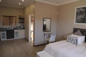a bedroom with a white bed and a kitchen at Andela Guesthouse in Bloemfontein